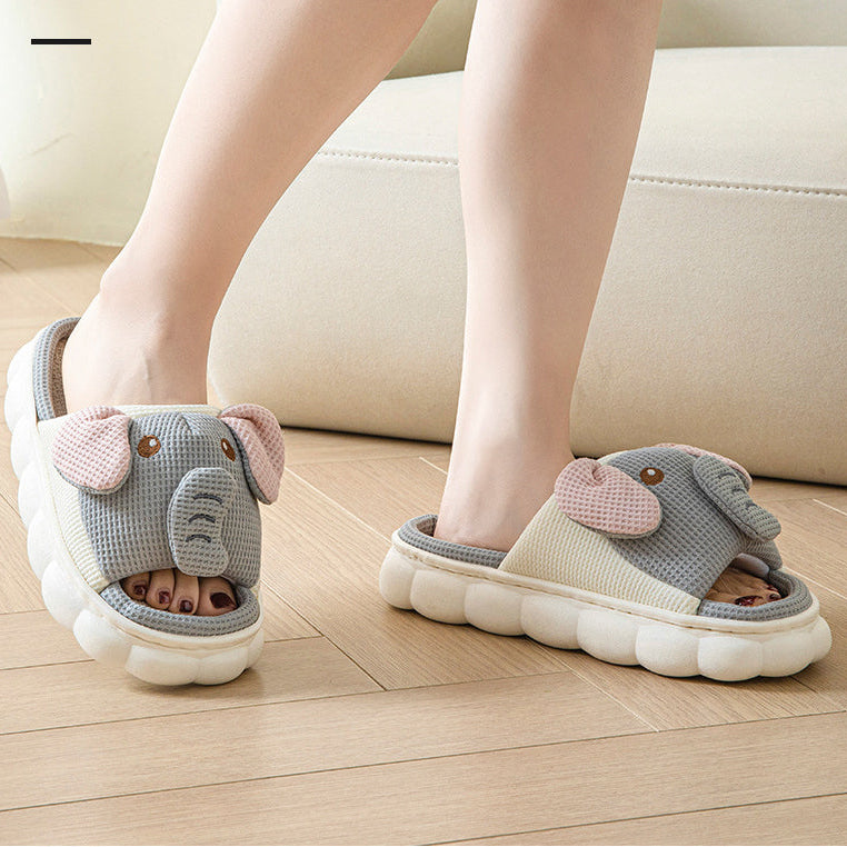 Children's kawaii elephant-themed slippers on a wooden floor with a beige sofa in the background.