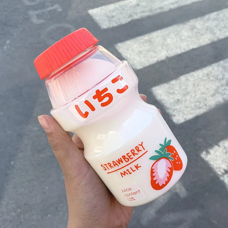 Hand holding a Kawaii strawberry milk bottle with a red cap against a blurred street background
