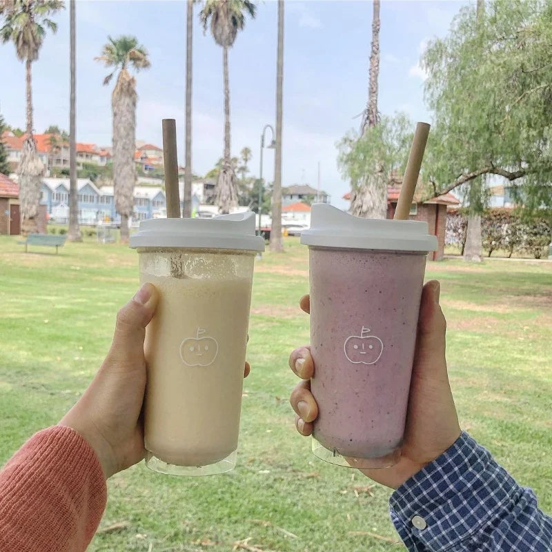 Two hands holding Kawaii-style cups with palm trees and a park in the background