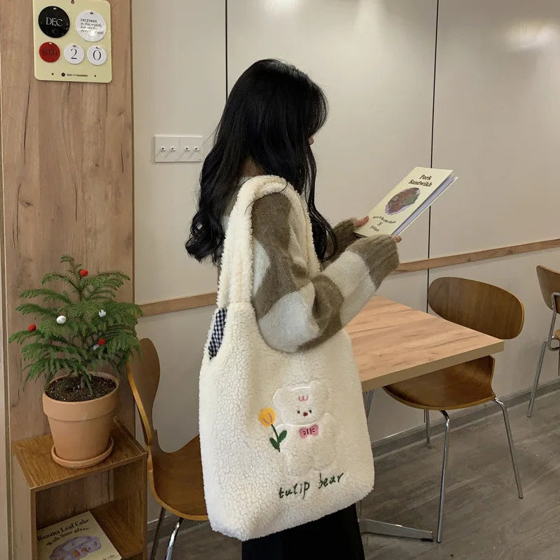 Person holding a plush bag with kawaii bear design in a room with wooden furniture and a plant.