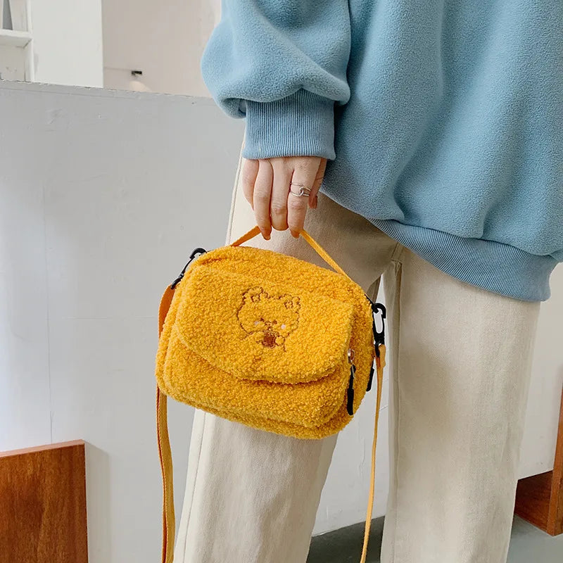 Person holding a yellow fluffy Kawaii bag with a bear design indoors.