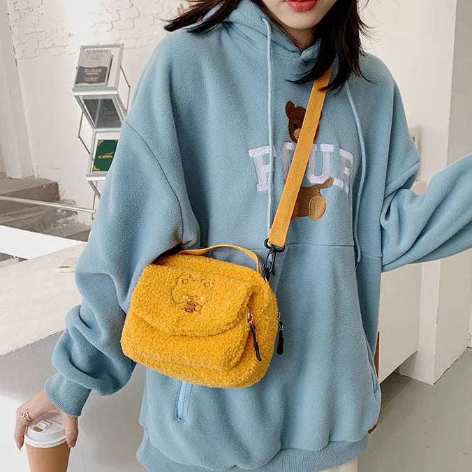 Person wearing a light blue hoodie with a Kawaii bear design, holding a yellow fluffy bag.