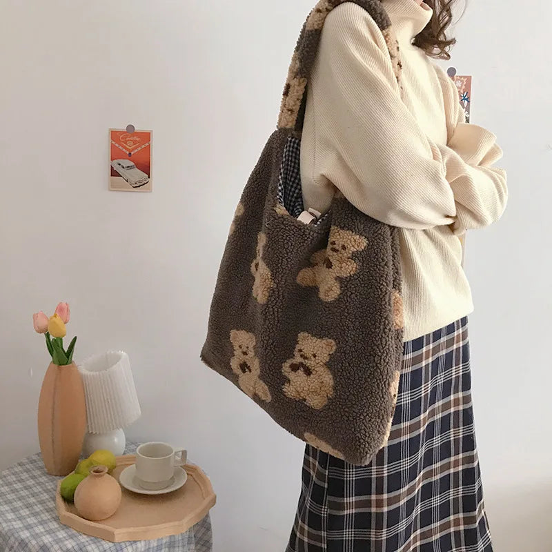Person holding a brown tote bag with kawaii teddy bear designs in a room setting.