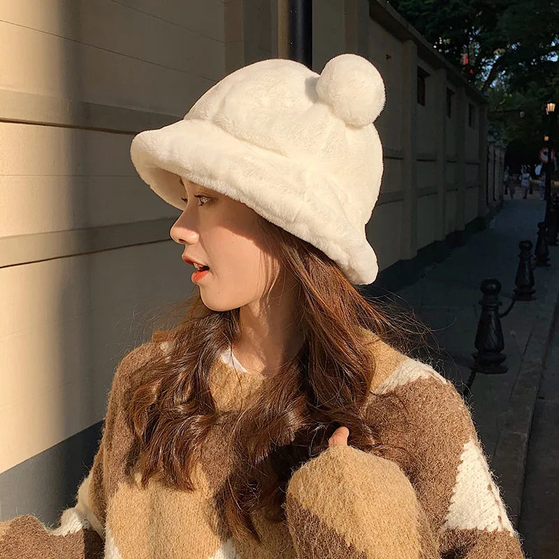 Woman wearing a white Kawaii fur hat with a pom-pom and a brown coat on a street.