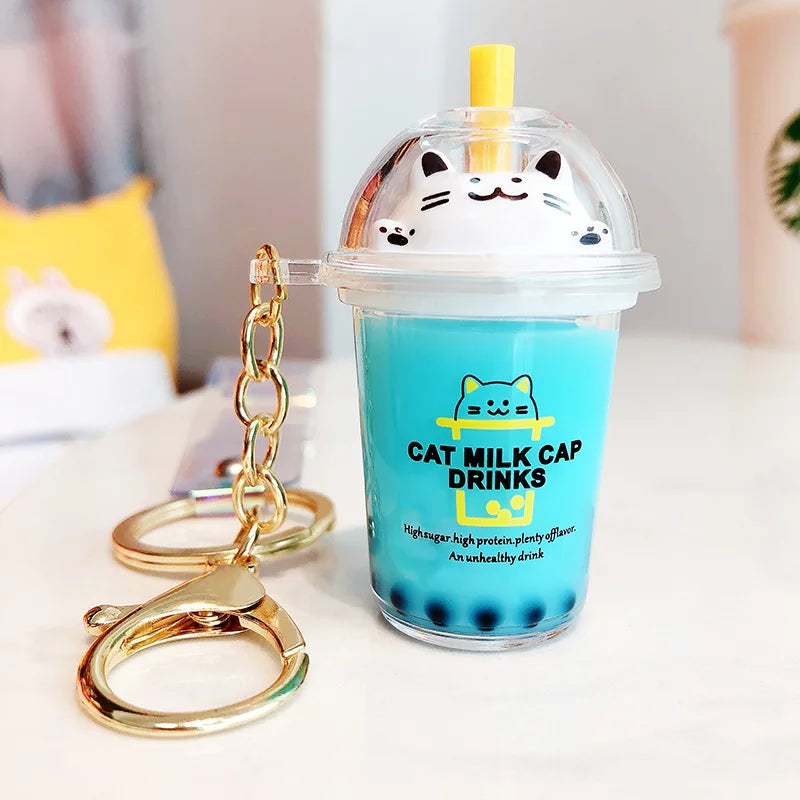 Cat-themed kawaii milk cap drink keychain with blue cup and gold chain on a white surface.