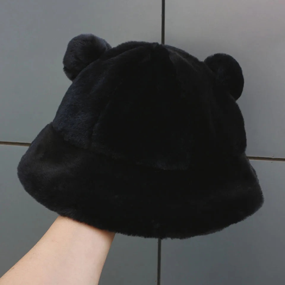 Black Kawaii fluffy hat with bear ears held by a hand against a gray tiled wall.
