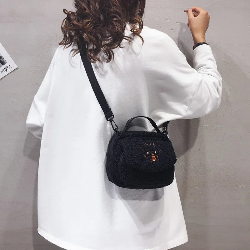 Person wearing a black textured handbag with a small Kawaii-inspired design on a plain background