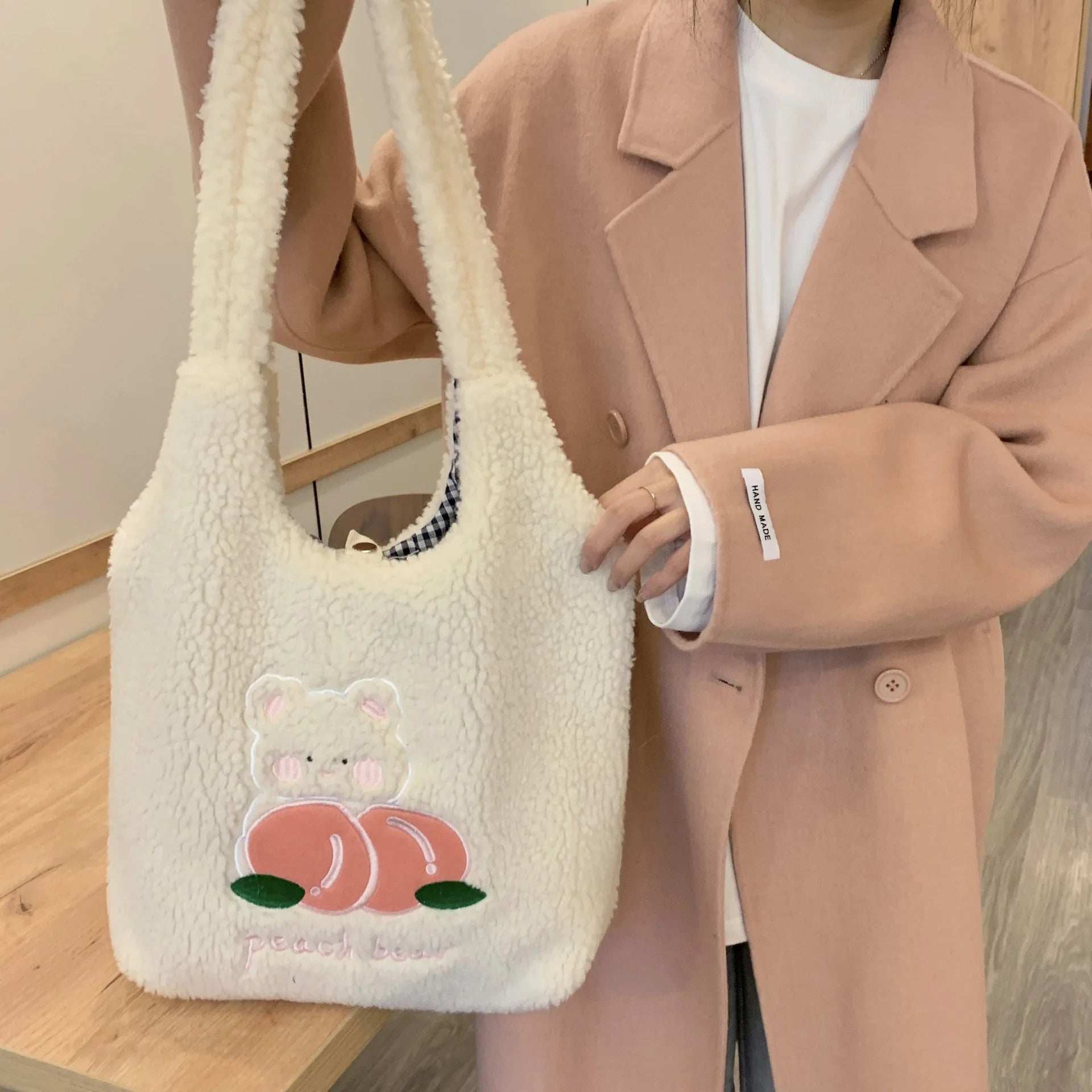 Person holding a fluffy white kawaii bag with a cartoon design, wearing a beige coat.