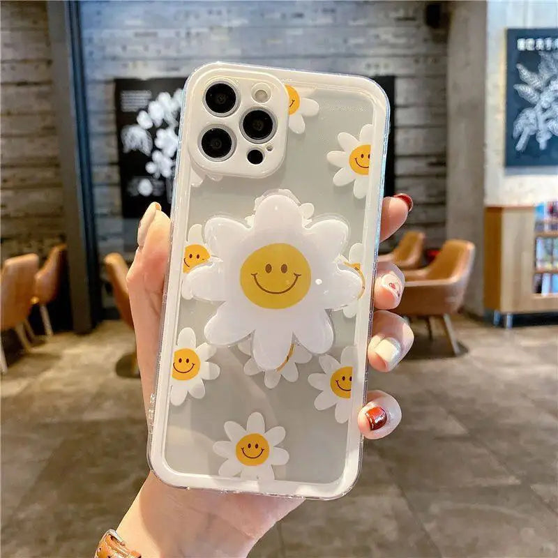 Phone case with kawaii smiley face daisy design held by a hand in an indoor setting.