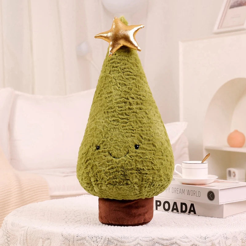 Green kawaii plush Christmas tree with a gold star on top, sitting on a surface with books and a cup in the background.