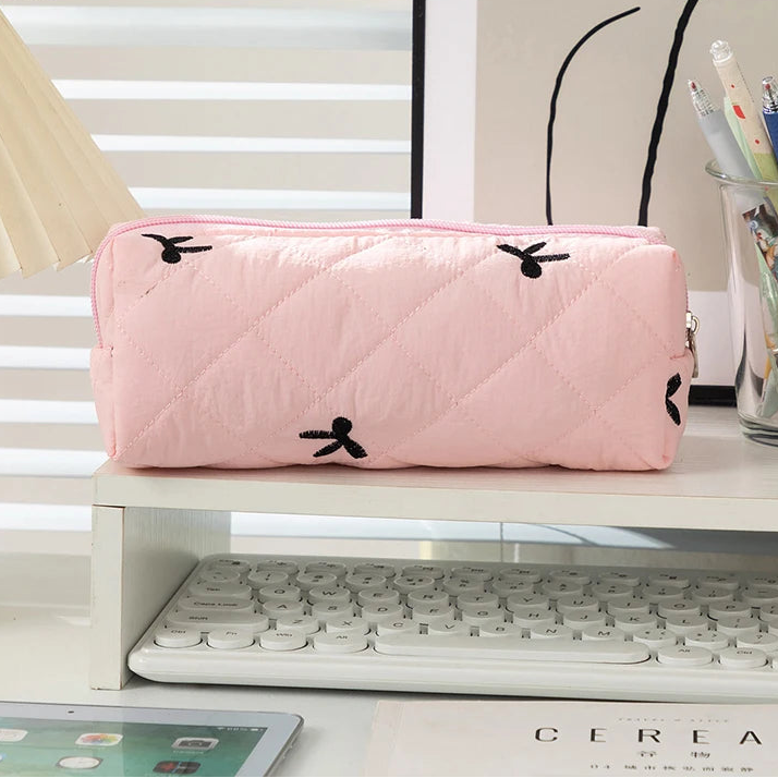 Pink quilted kawaii pencil case on a desk with a keyboard and stationery items.