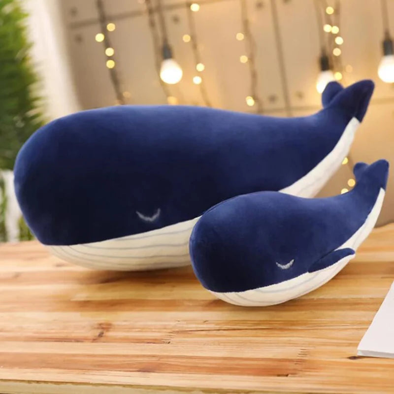 Two blue whale-shaped kawaii pillows on a wooden surface with a blurred background