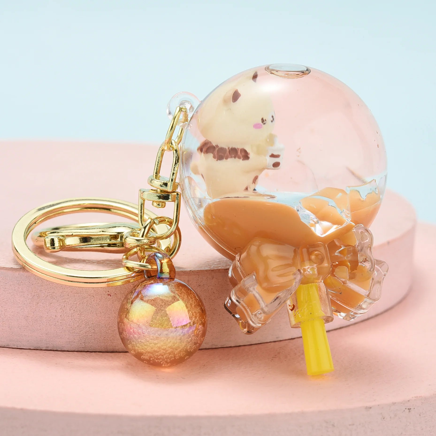 Keychain with a transparent holder featuring a kawaii cartoon character, gold ring, and orange ball on a light blue background.