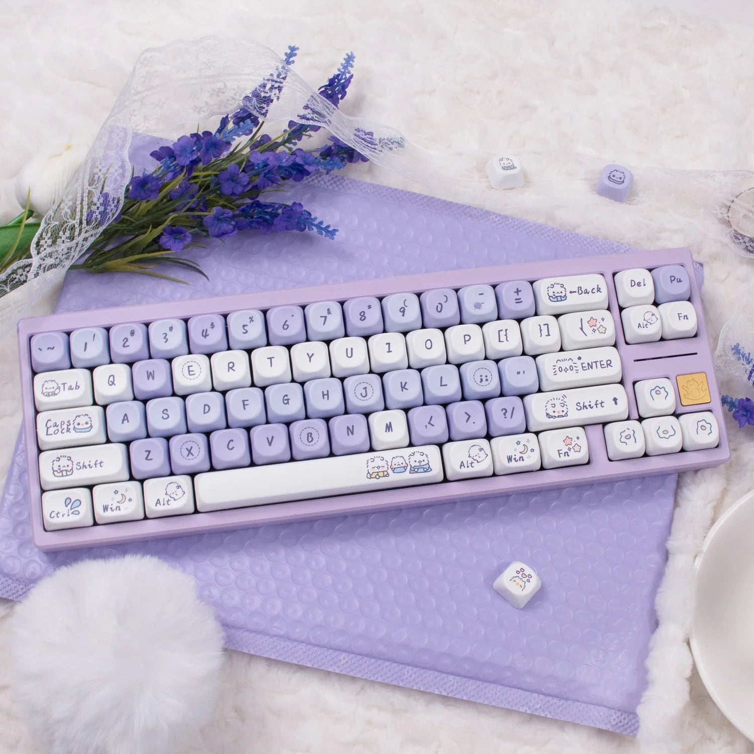 Purple keyboard with Kawaii character keys on a soft purple surface with flowers