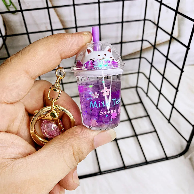 Keychain shaped like a kawaii purple milk tea cup with a cat design, held by a hand.