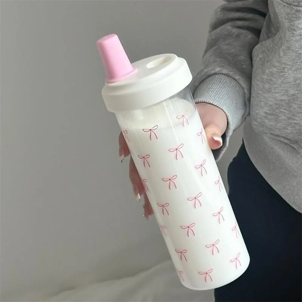 White Kawaii sippy cup with pink lid and bow pattern held by a person against a neutral background