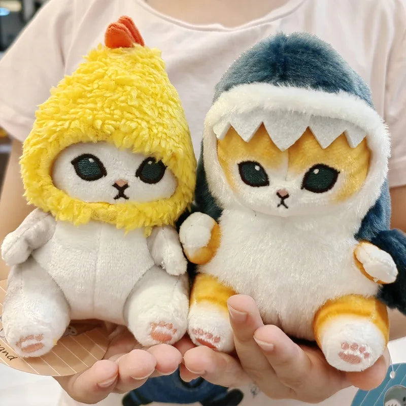 Two kawaii plush toys resembling cats with colorful hats held by a person.