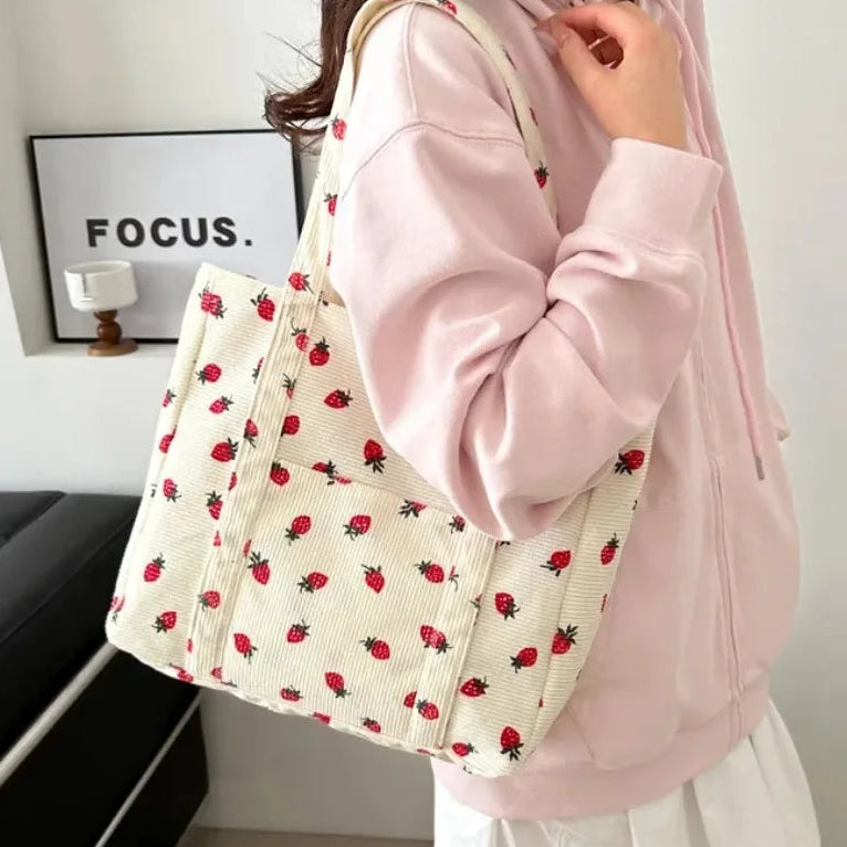 Person holding a tote bag with strawberry kawaii pattern in a minimal indoor setting