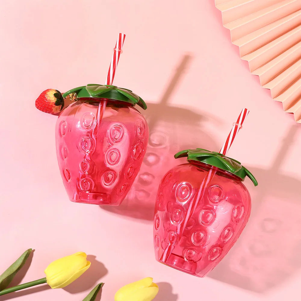 Two Kawaii strawberry-shaped drink containers with straws on a pink background