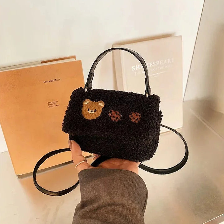 Black furry handbag with Kawaii bear face design held by a person, with books in the background.