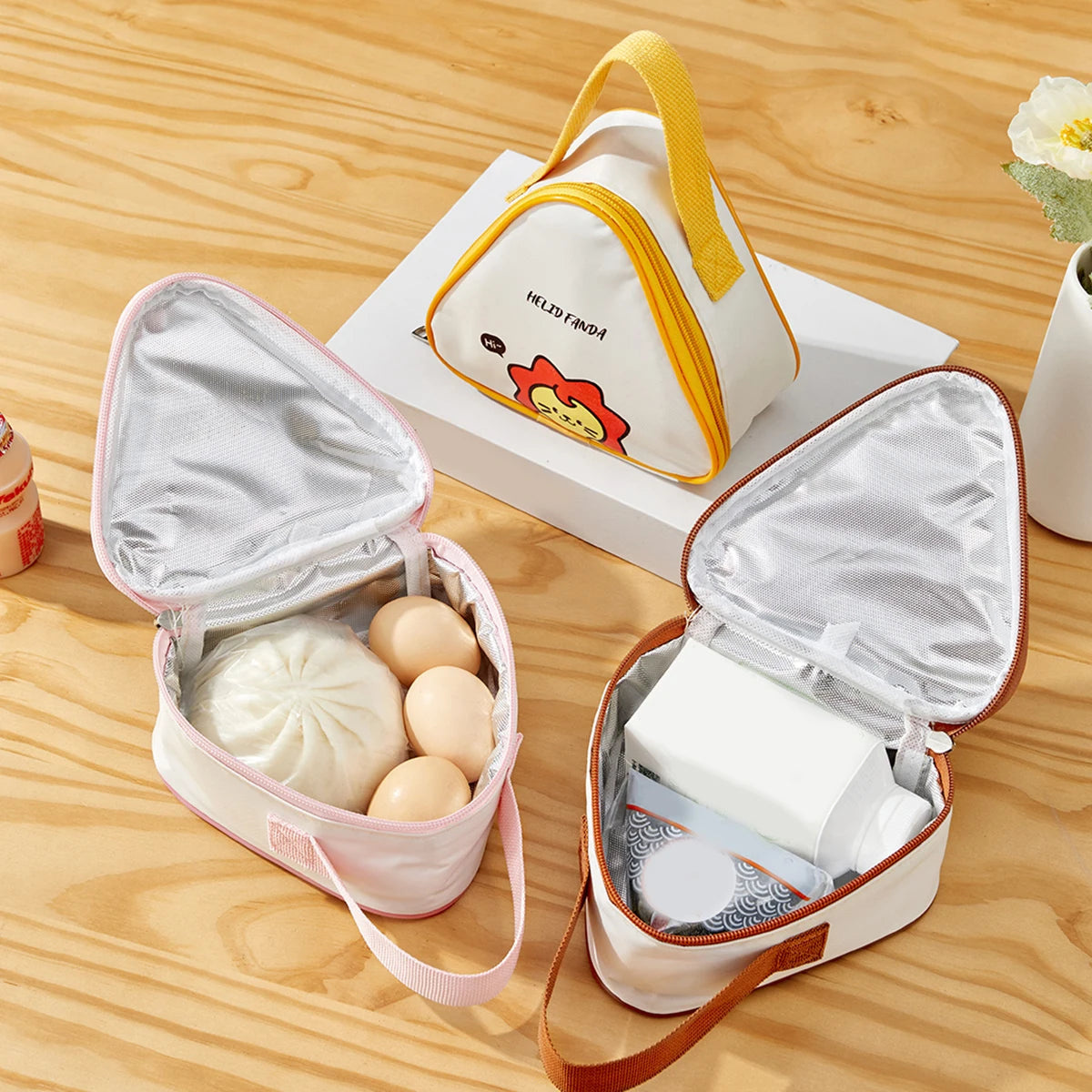 Two insulated kawaii-style lunch bags on a wooden surface with food items inside.