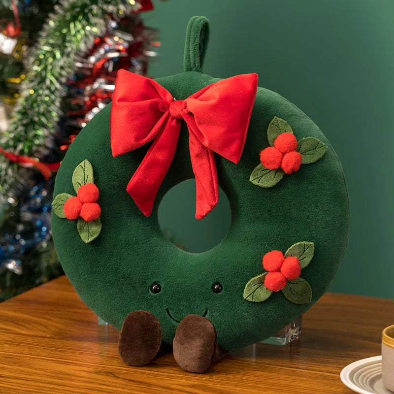 Green kawaii plush wreath with a red bow and holly leaves on a wooden surface.