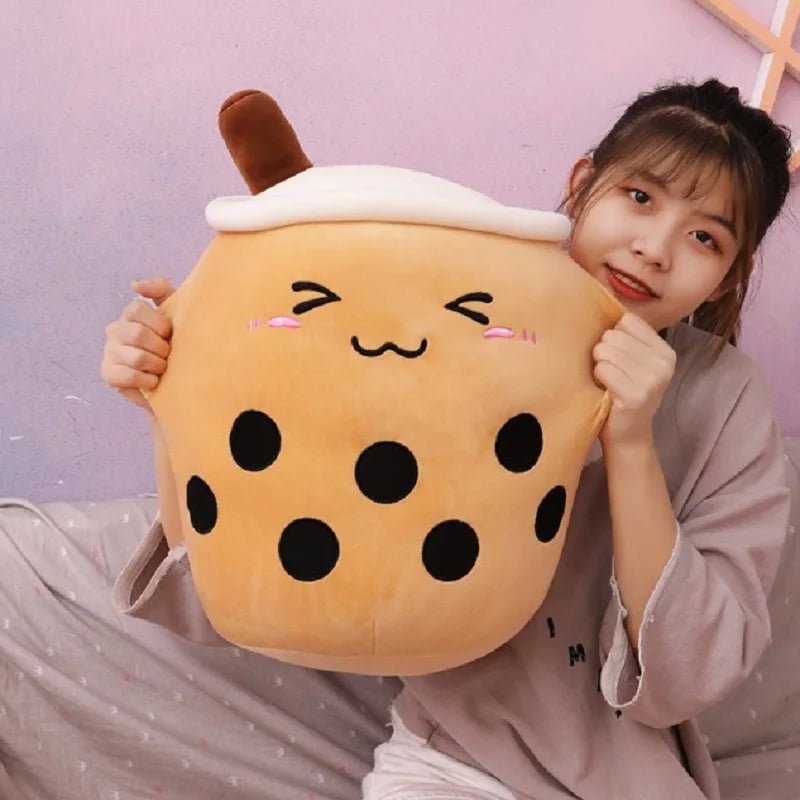 Person holding a plush kawaii toy shaped like a bubble tea cup with a smiling face against a pink background