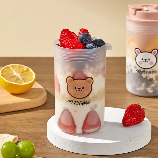 Transparent tumbler with a Kawaii bear design filled with fruit on a wooden surface.