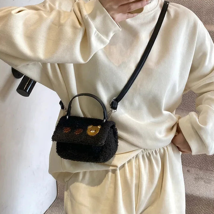 Person wearing a black textured Kawaii handbag with a gold clasp on a plain background