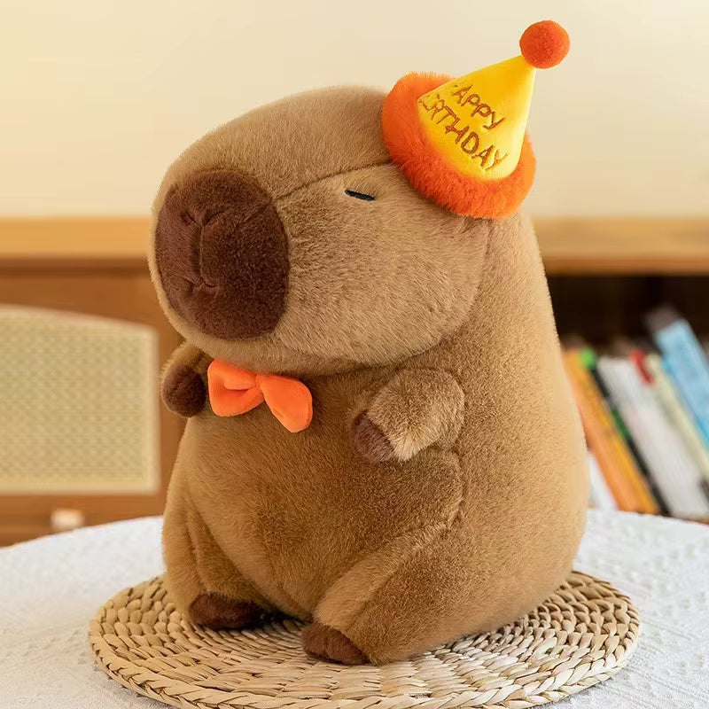 Kawaii plush toy animal wearing a party hat with 'Happy Birthday' text on a woven mat.