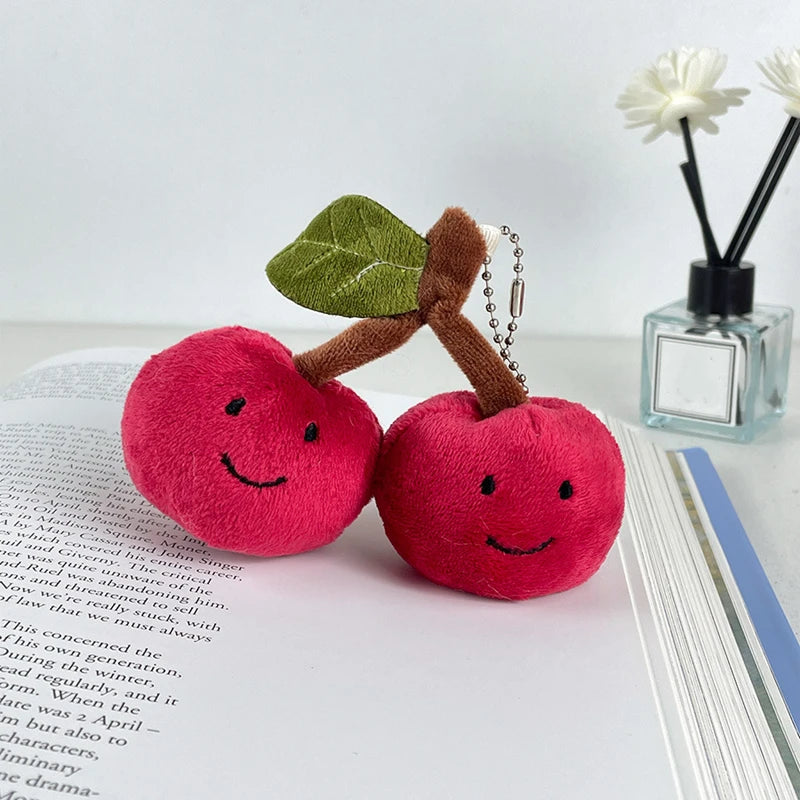 Two plush kawaii cherries with faces on a book next to a small bottle of essential oils.