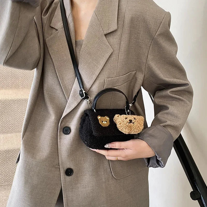 Person wearing a beige suit holding a black handbag with a Kawaii teddy bear design.