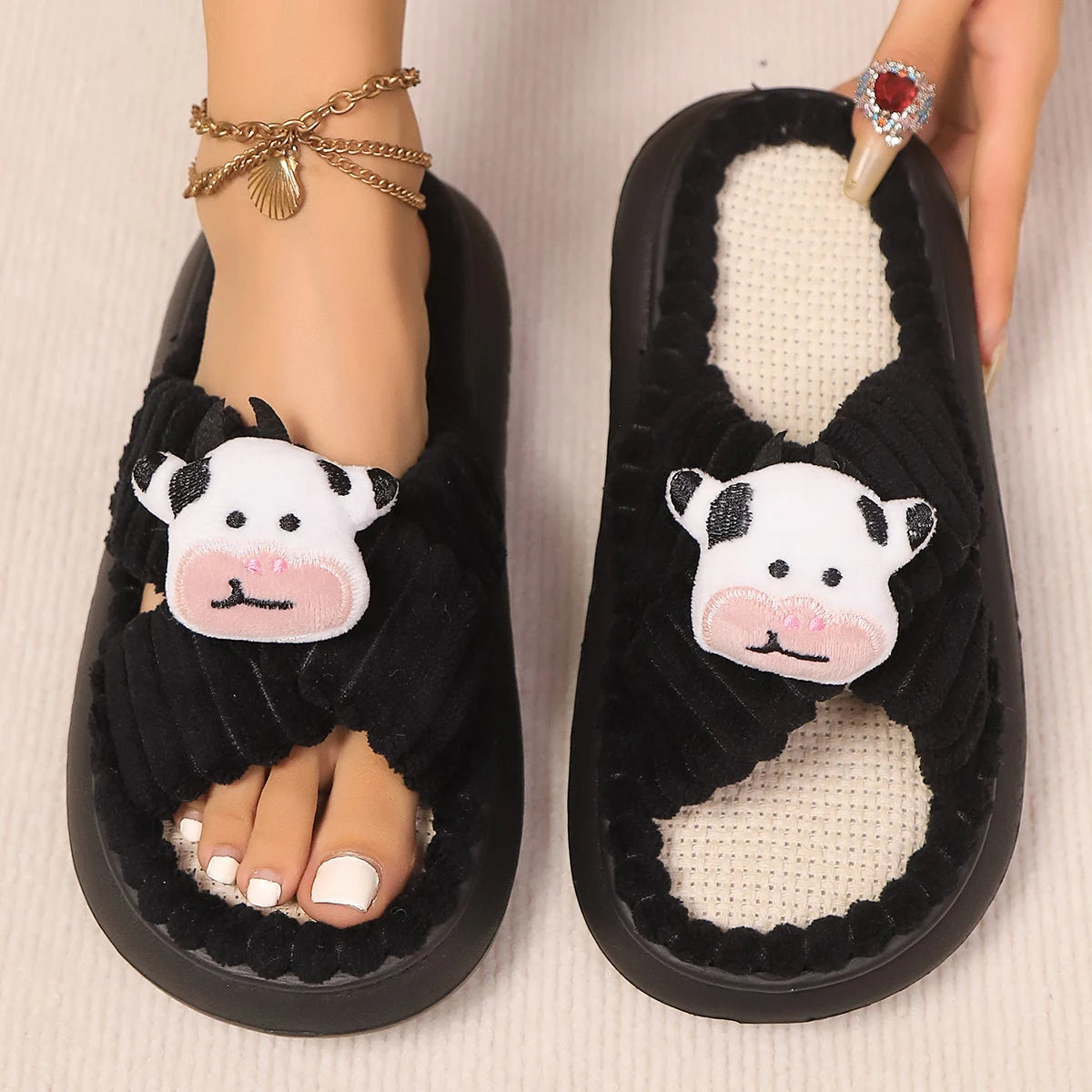 Black slippers with kawaii cow face design worn by a person on a light background