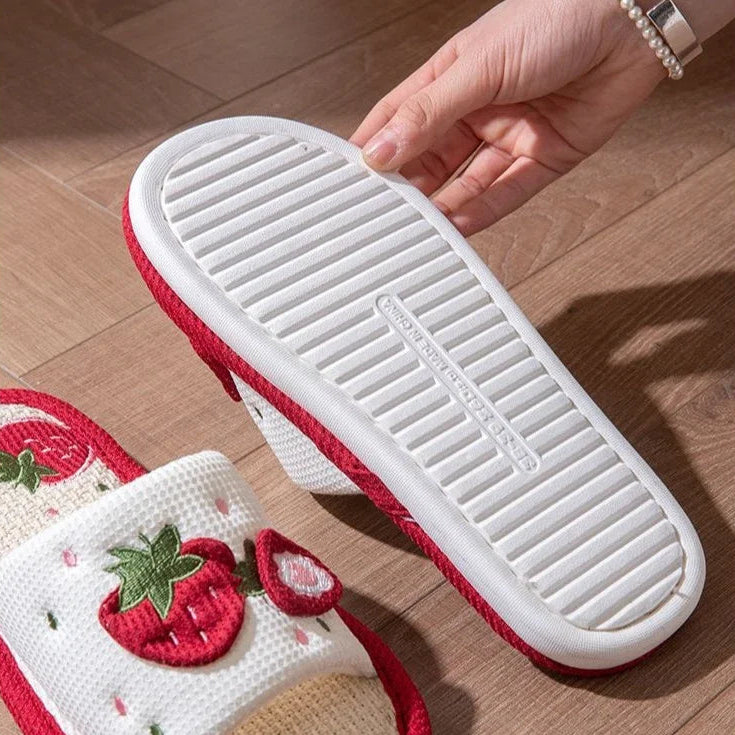 White slippers with red accents and strawberry kawaii design on a wooden floor.