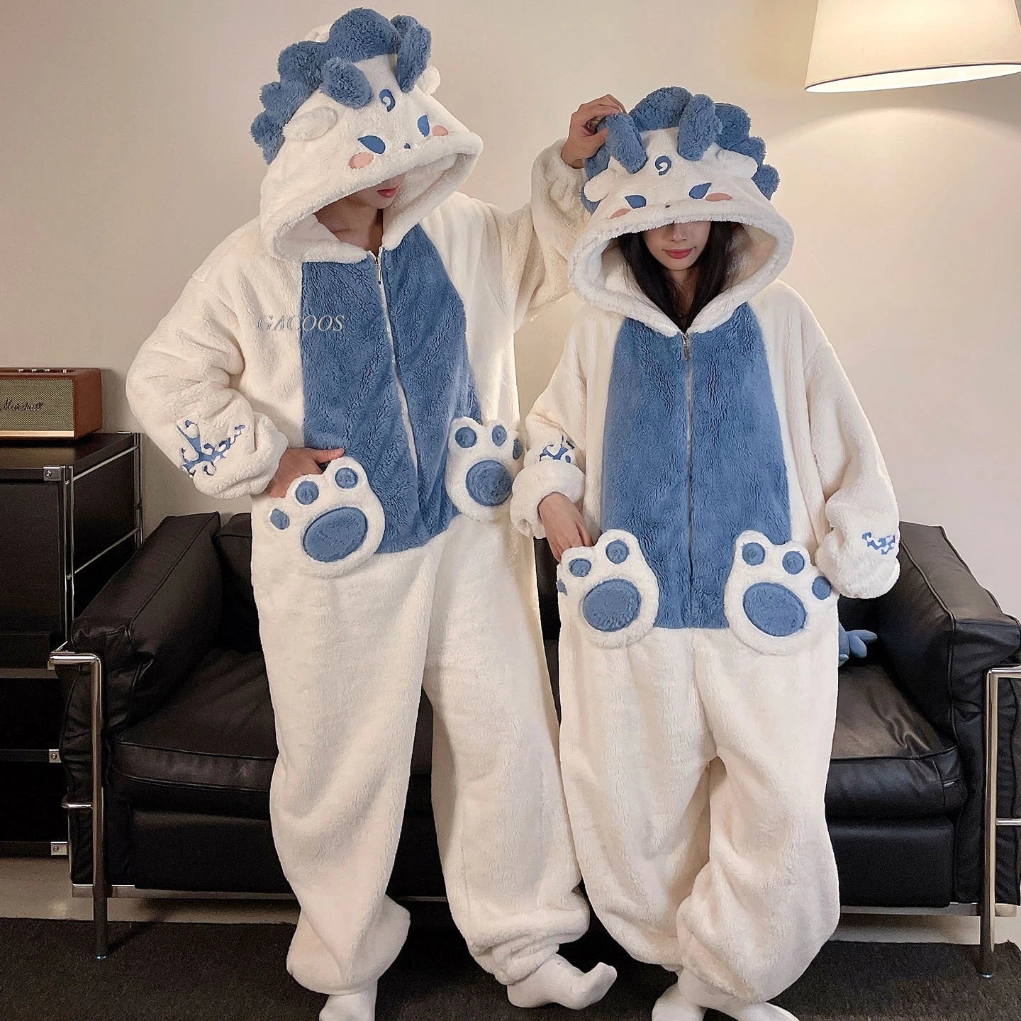 Two people wearing matching blue and white kawaii onesies with animal design in a living room.