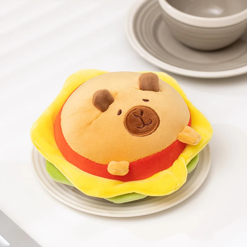 Plush toy shaped like a kawaii bear in a hamburger on a white plate with a bowl in the background.