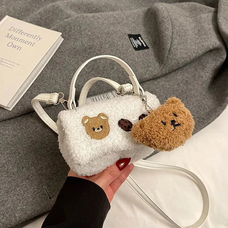 Small white fluffy bag with Kawaii bear design held by a hand on a gray surface.