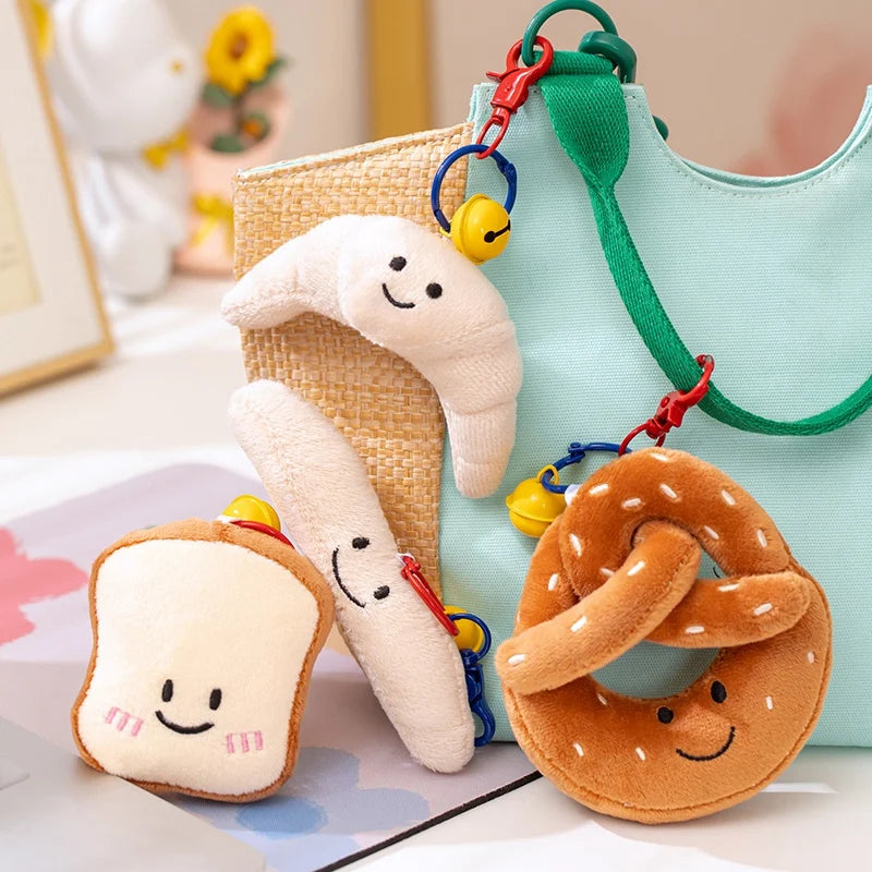 Plush kawaii toys shaped like a pretzel, bread, and a cloud with a bell, attached to a green strap.