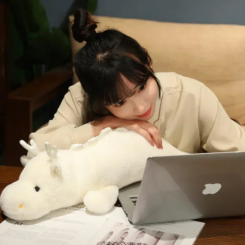 Woman lying on a couch with a kawaii plush toy and laptop, wearing a beige shirt.