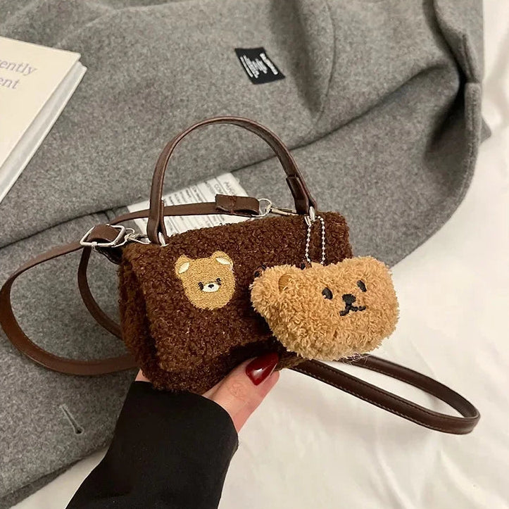 Brown Kawaii teddy bear-themed handbag with matching keychain held by a hand against a gray fabric background.