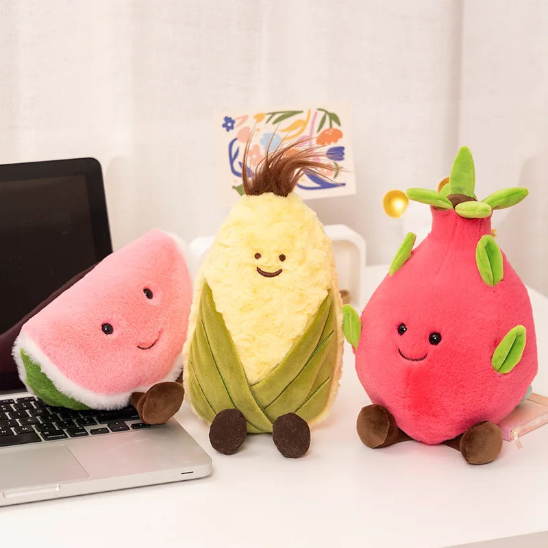 Three plush kawaii toys shaped like a watermelon, pineapple, and dragon fruit on a desk with a laptop.