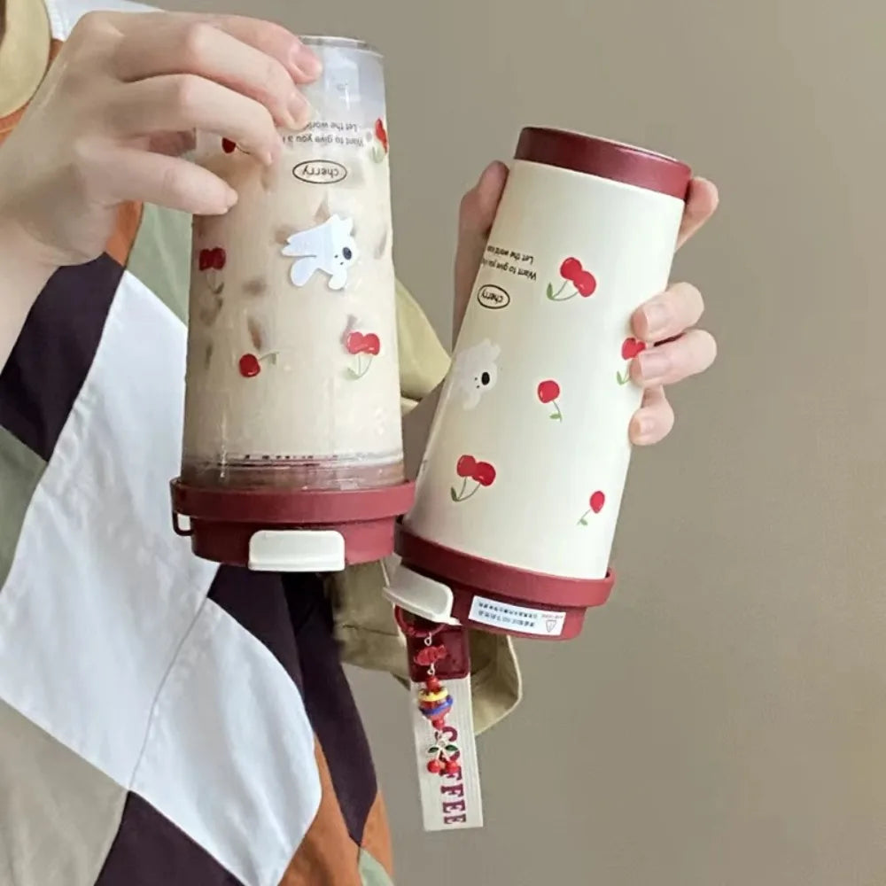 Two Kawaii cartoon-themed tumblers with cherry designs held by a person against a neutral background.