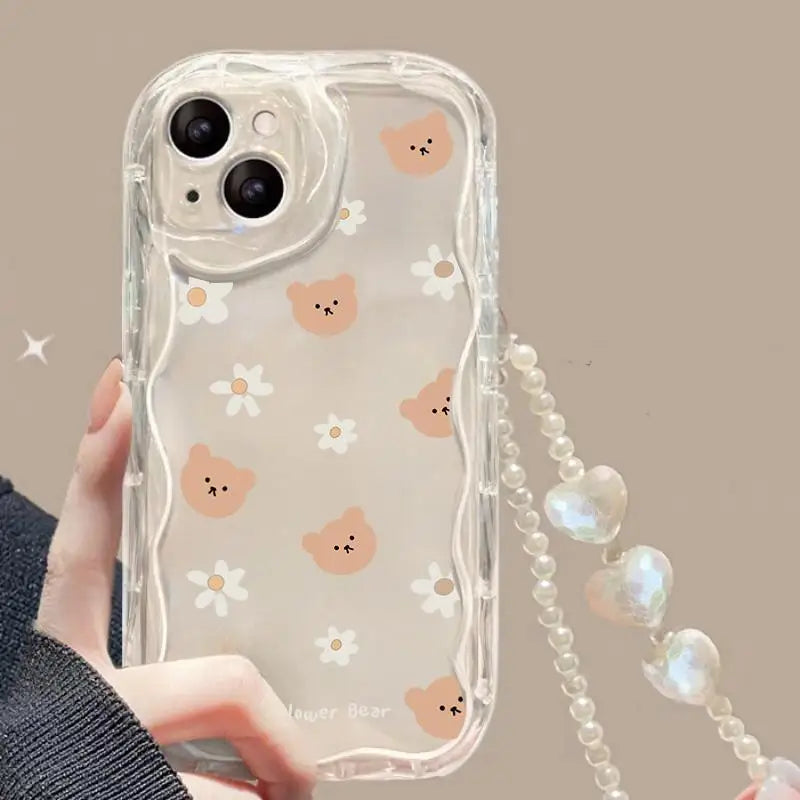 Phone case with kawaii bear and flower pattern and heart-shaped strap held by a hand.
