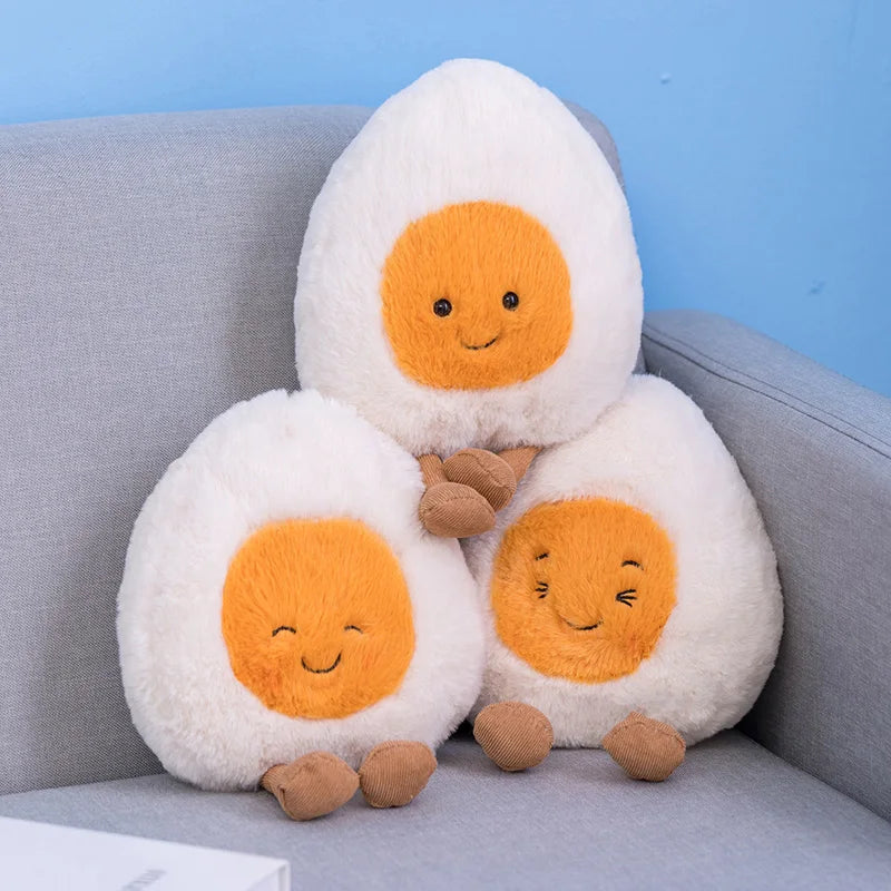 Three plush kawaii toys shaped like boiled eggs with smiling faces on a gray couch.