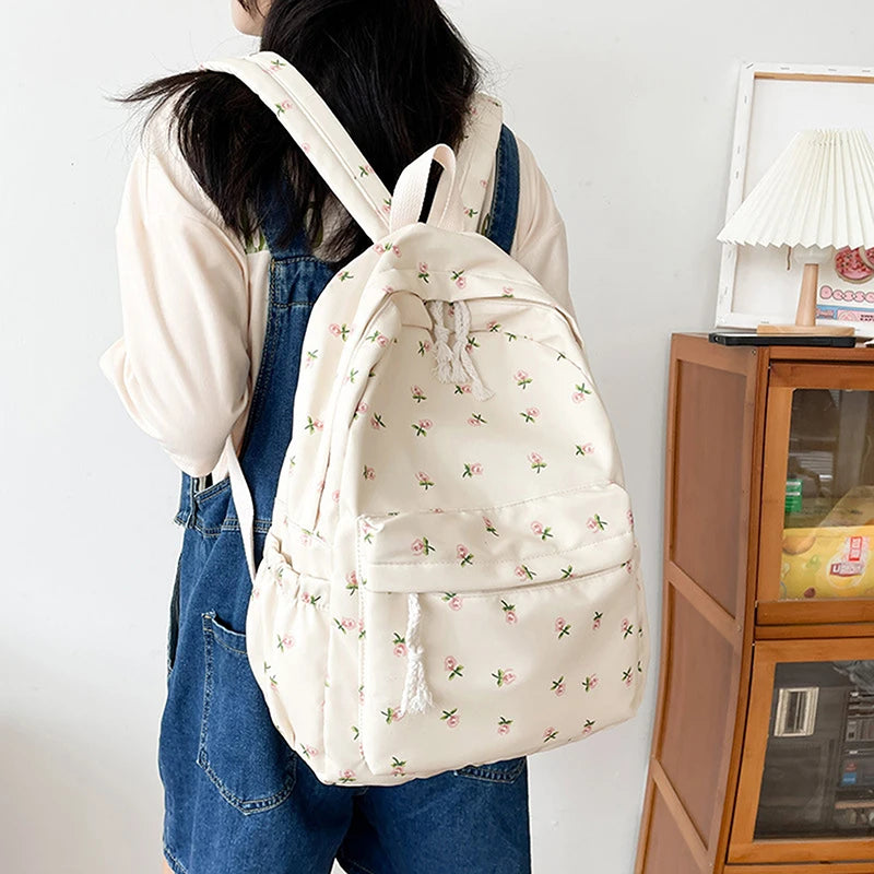 Person wearing a white Kawaii floral backpack in a room with a wooden cabinet and lamp.