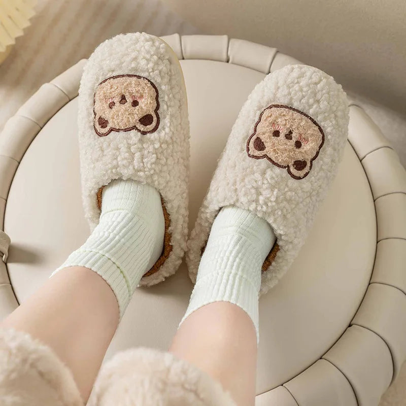 Pair of fluffy slippers with kawaii cartoon face design worn by a person sitting on a white chair.