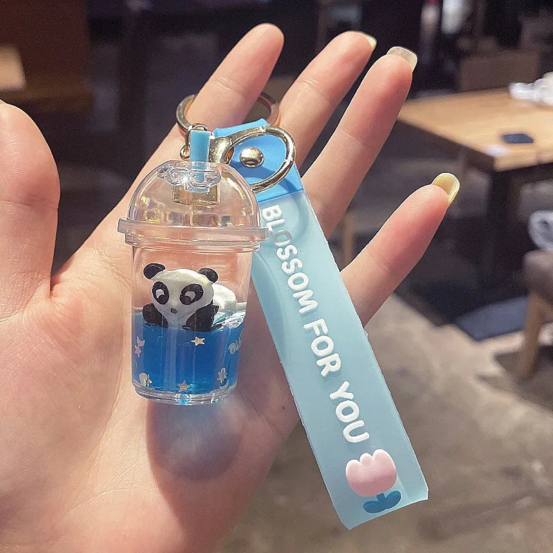 Clear cup-shaped kawaii keychain with panda figure and blue tag held in a hand.