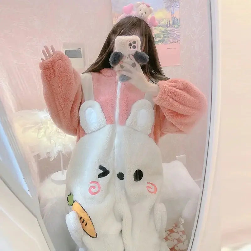 Person wearing a pink fluffy kawaii sweater with cartoon character design, holding a plush toy.