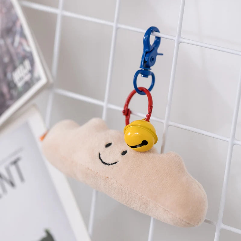 Plush cloud-shaped kawaii keychain with a smiley face and yellow bell on a white tiled wall background.