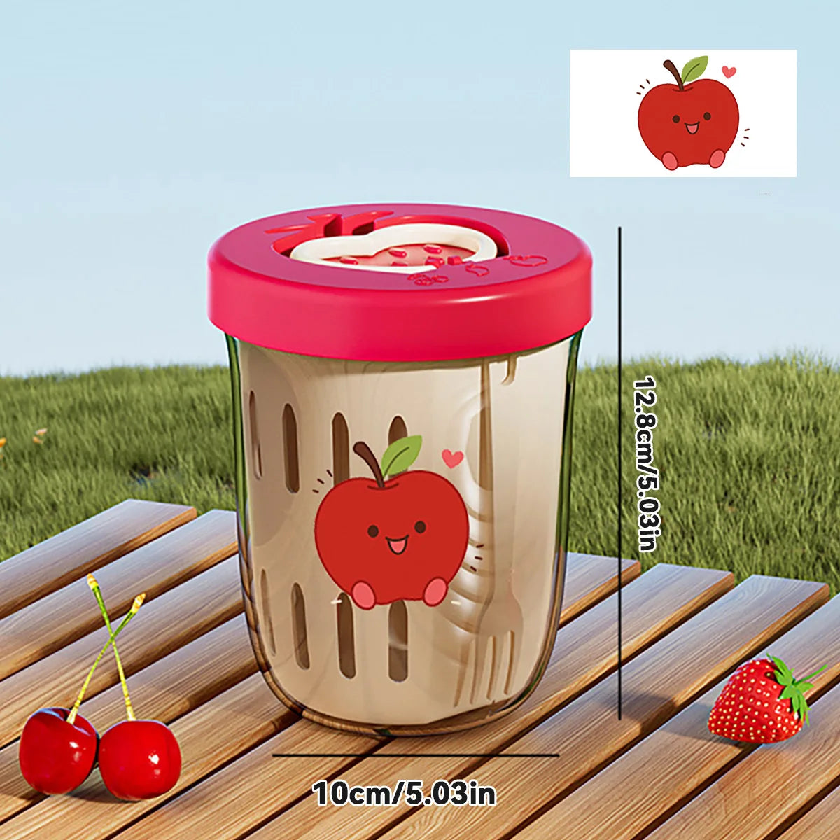 Clear tumbler with red lid and Kawaii apple design on a wooden surface with grass in the background